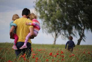 Dad holding children in field.